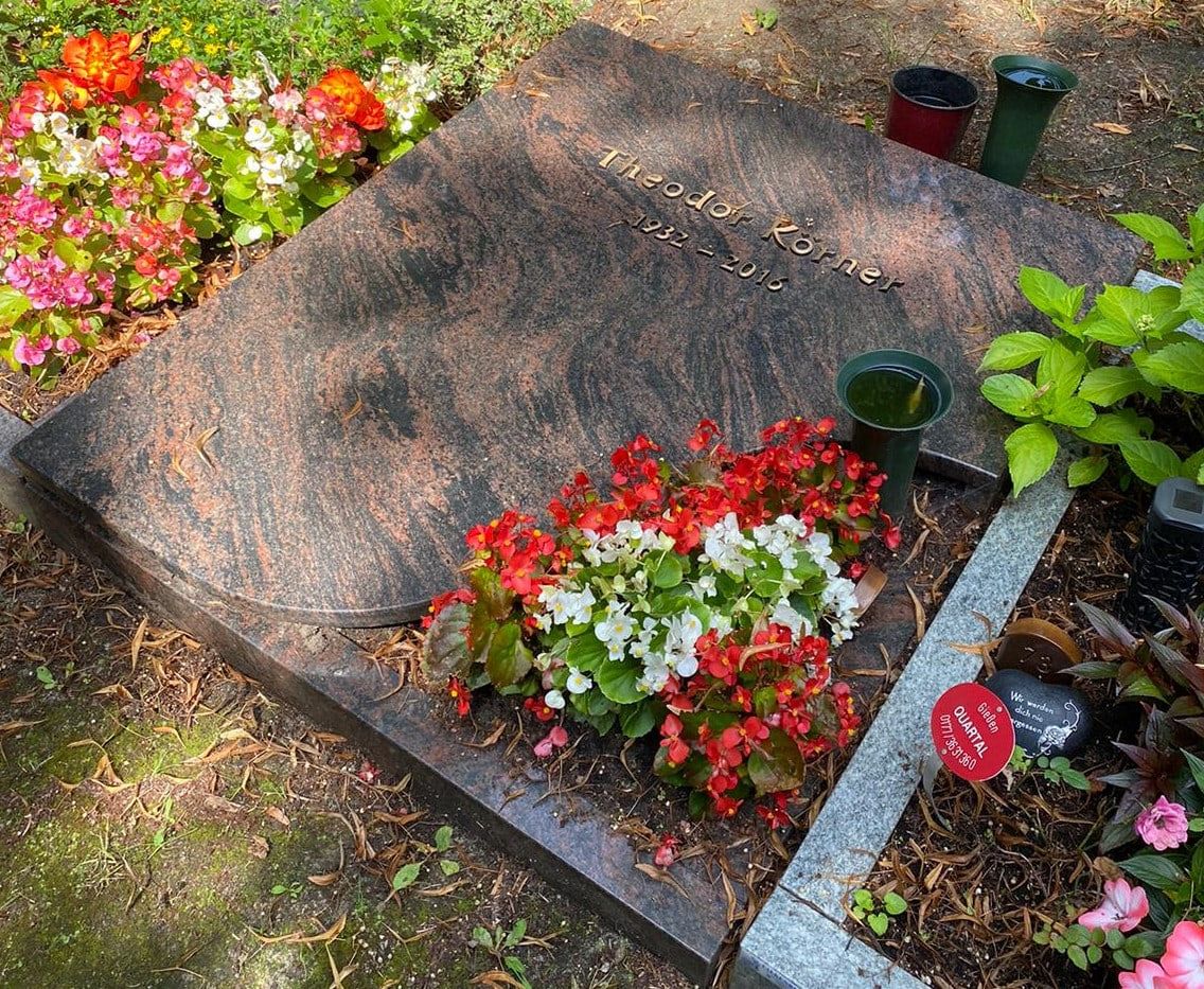Polished reddish-brown grave slab with flowers, planters and memorial candles at Kaulsdorf Cemetery
